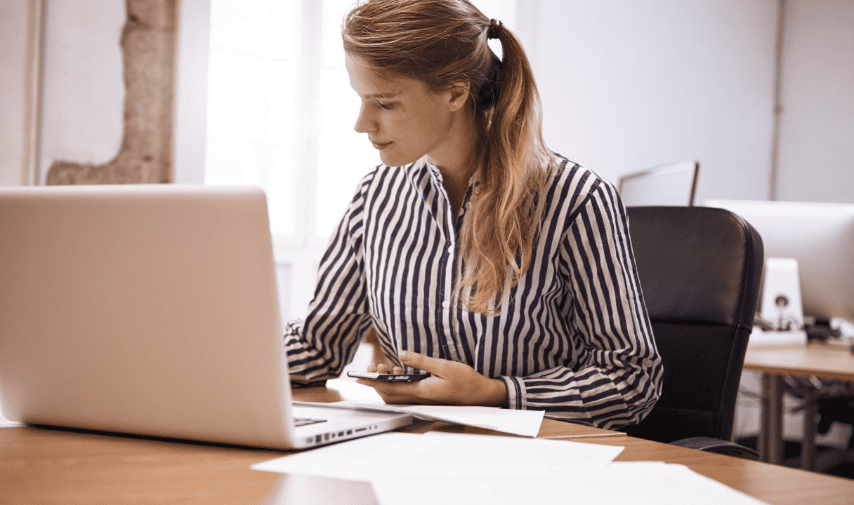 Woman working on her laptop while having a phone in her hand